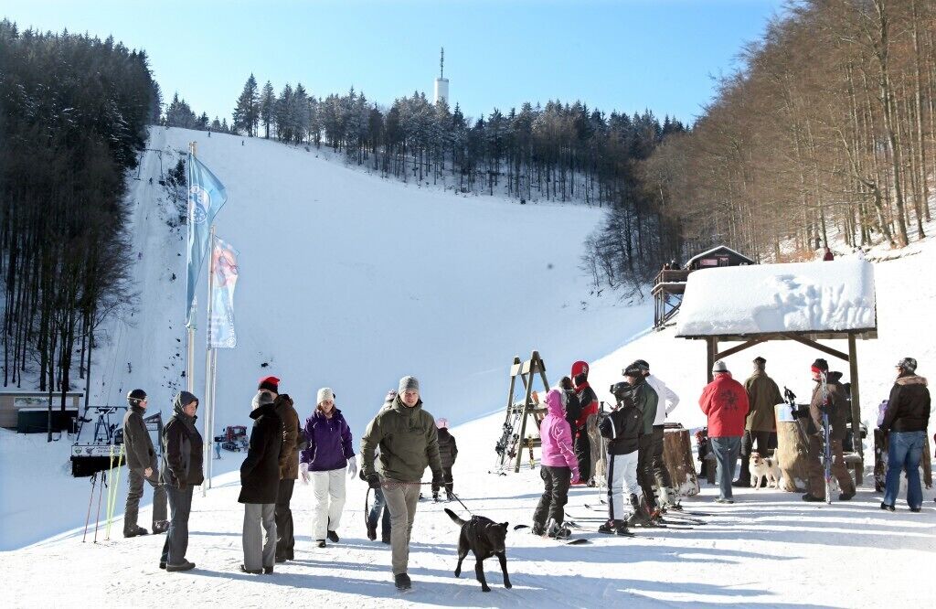 A group of people on a snowy slope with a ski lift and a wooden shelter.