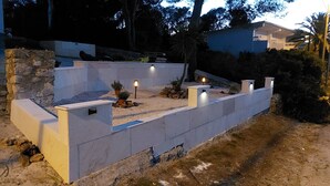 Un patio exterior moderno con pared de piedra, asientos e iluminación decorativa.