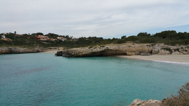 Un paisaje costero con aguas turquesas cristalinas, una playa arenosa y acantilados rocosos.