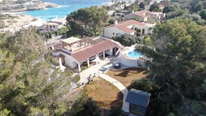 Vista aérea de una propiedad costera con piscina, varias construcciones y follaje circundante.