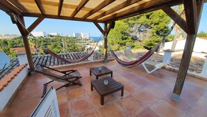 Un patio cubierto con una hamaca, sillas de madera para lounge y piso de baldosas.