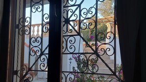 Una reja de hierro forjado con diseños intrincados, que da acceso a un balcón con vistas a un edificio con columnas y una pérgola.