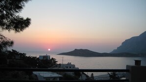 Ein Sonnenuntergangsblick vom Balkon mit Blick auf ein Gewässer, im Hintergrund Gebäude und ein Berg.
