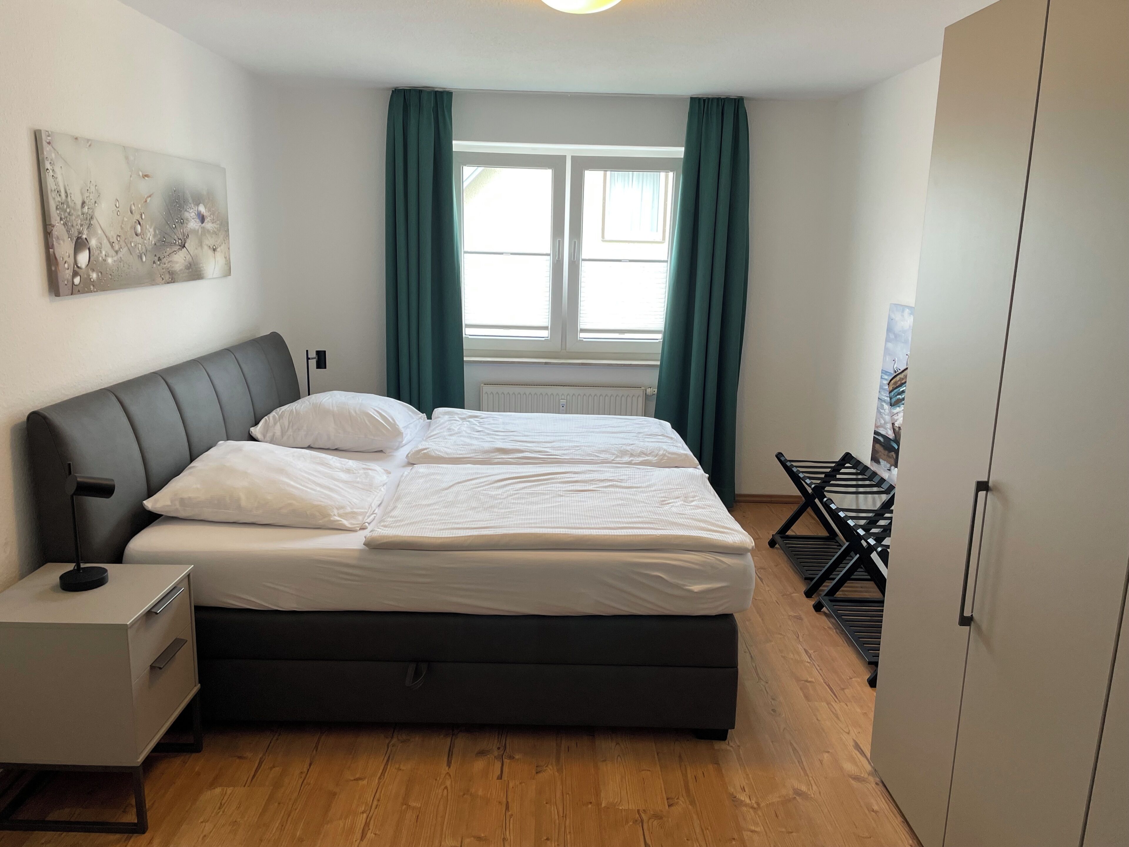 Ein Schlafzimmer mit einem Bett, einem Nachttisch, einer Kommode, einer Heizung und einem Fenster mit Vorhängen.