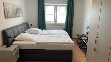 Ein Schlafzimmer mit einem Bett, einem Nachttisch, einer Kommode, einer Heizung und einem Fenster mit Vorhängen.