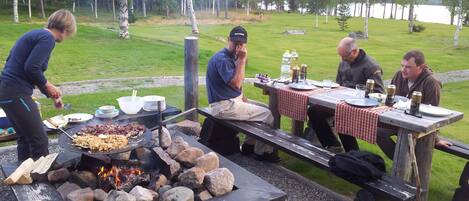 Un grupo de personas reunidas alrededor de una parrilla al aire libre, con un lago al fondo.