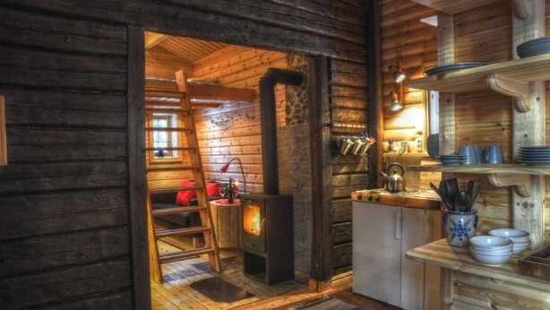A cozy cabin interior with a wooden interior, a kitchen area with a stove, and a ladder leading to a loft bed. - Quaint holiday home in the forests of Lapland by the river (Sorsele)