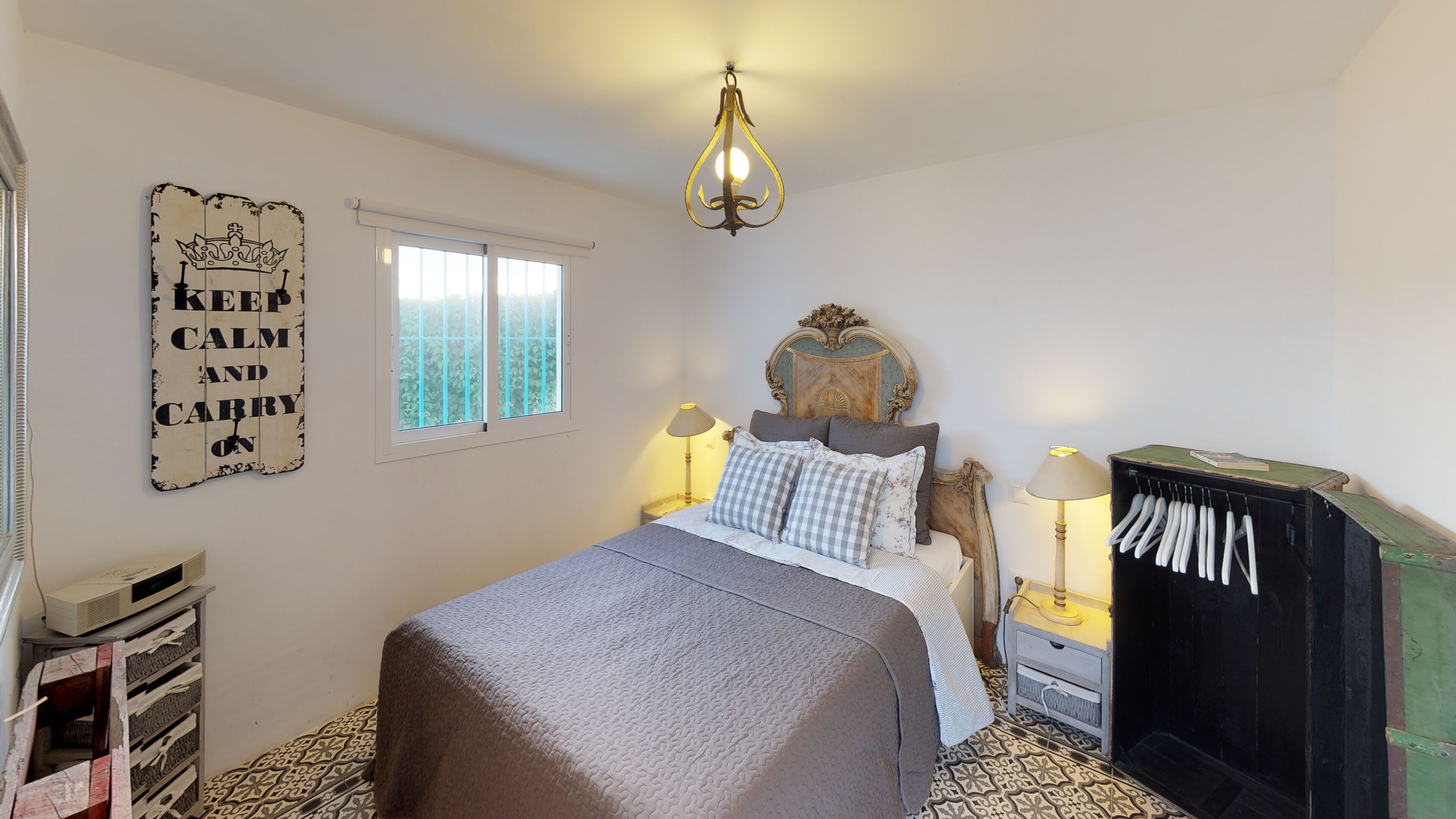 Een slaapkamer met een bed, twee nachtkastjes, een hanglamp, een garderobe, een raam en een decoratief bord aan de muur.
