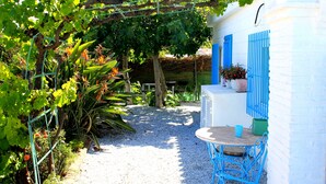 Ein Garten mit Tisch und Stühlen, einer mit Kletterpflanzen bewachsenen Pergola und einem weißen Gebäude mit blauen Fensterläden.