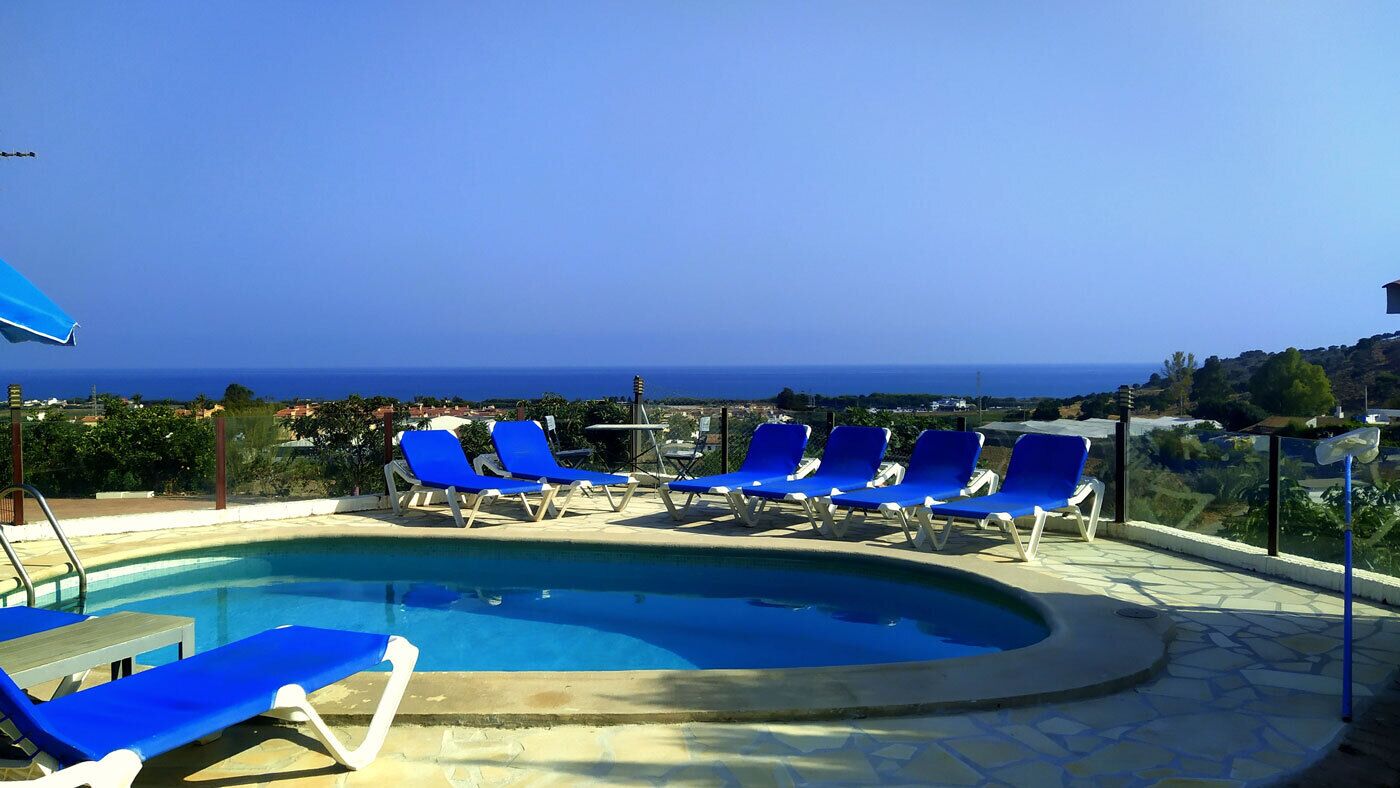 A pool area with blue lounge chairs and a view of the sea.