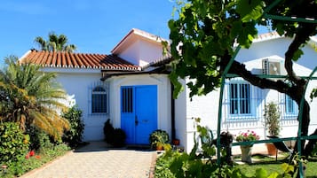 Un edificio bianco con una porta e finestre blu, immerso nel verde e con un vialetto lastricato.