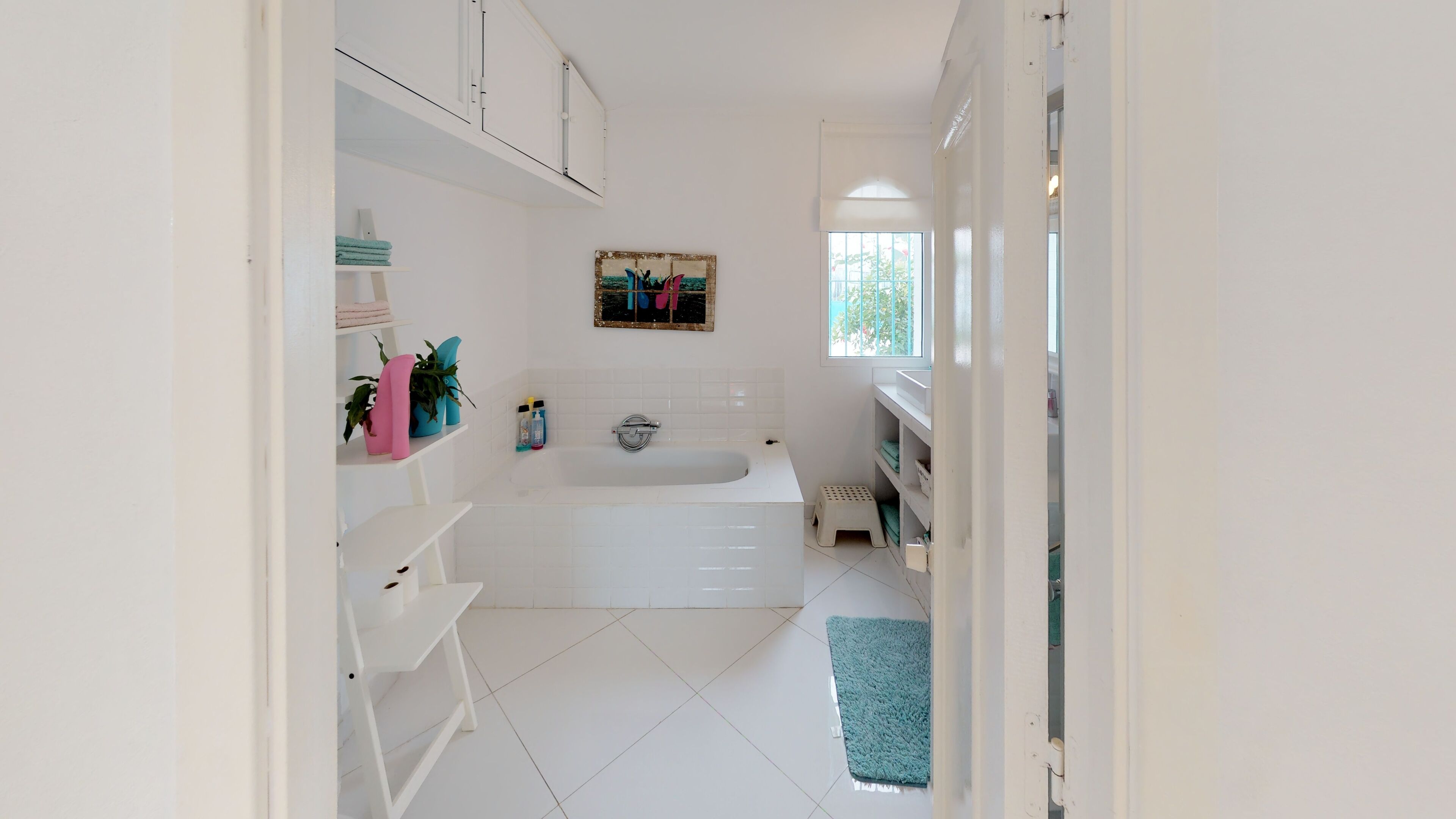 Une salle de bain moderne avec une baignoire blanche, des étagères contenant des articles de toilette et une fenêtre laissant entrer la lumière naturelle.