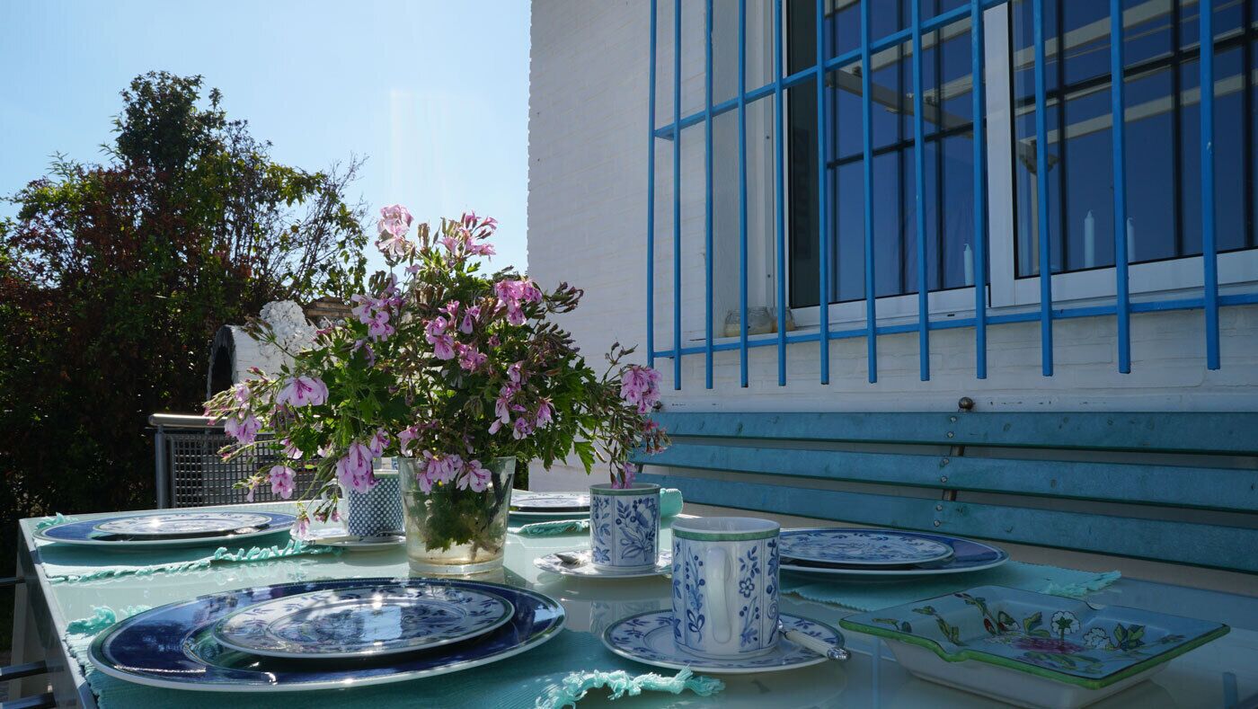 Uma mesa posta com pratos azul e branco, um vaso com flores rosa e uma xícara com padrão azul e branco.