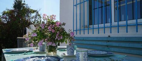 Uma mesa posta com pratos azul e branco, um vaso com flores rosa e uma xícara com padrão azul e branco.