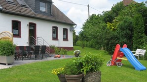 Ett hus med en röd och blå rutschkana, en liten trädgård med krukväxter och utemöbler.