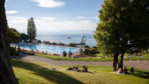 Zona de piscina con vista al mar, rodeada de césped y árboles.