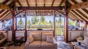 Una habitación acogedora con techo de madera, un sofá y vistas a árboles a través de amplias ventanas.