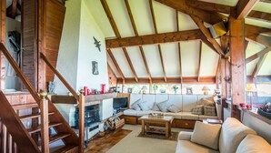Un salón acogedor con techo alto, vigas de madera, chimenea, sofá y escalera.