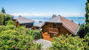 Un edificio de estilo chalet con fachada de madera y techo inclinado, rodeado de vegetación exuberante y con vistas a un lago.