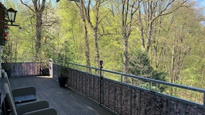 A wooden deck with stone walls, wicker chairs, and a lantern. - Villa Warzenburg, apartment 2 with panoramic view, balcony and fireplace. Vacation with a dog. (Friedrichroda)