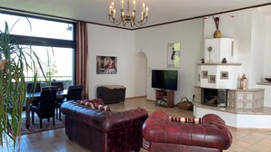 A living room with a large TV, a fireplace, and a dining area with a table and chairs. - Villa Warzenburg, apartment 2 with panoramic view, balcony and fireplace. Vacation with a dog. (Friedrichroda)