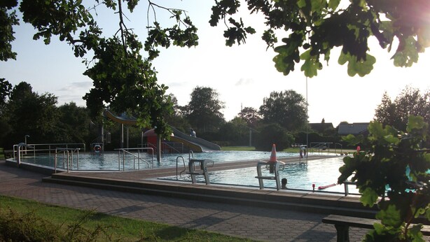 Ein Swimmingpool mit Rutsche, umgeben von einem Pflasterweg und Grünflächen.