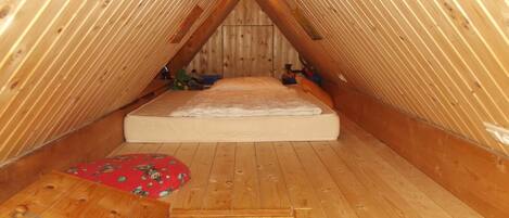 Un pequeño dormitorio de áticos con techo inclinado, una cama individual, una mesita y muebles de madera.