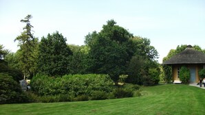 Ein gepflegter Garten mit einem Strohdachgebäude, umgeben von üppiger Vegetation und einer Rasenfläche.