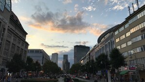 Eine Stadtstraße mit modernen Gebäuden, blauem Himmel und einigen Fußgängern.