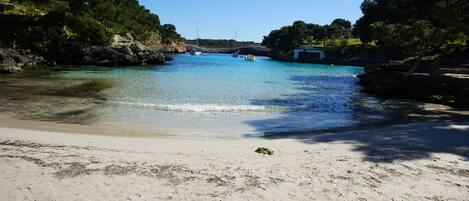 A beach with clear turquoise water, sandy shore, and rocky cliffs.