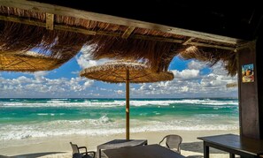 A beachside seating area with thatched umbrellas, a view of the ocean, and a sandy beach.