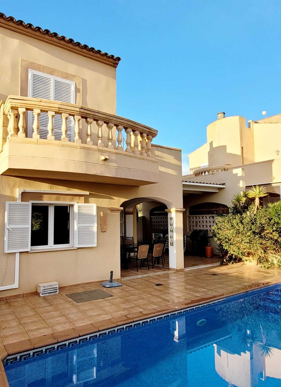 A two-story house with a pool, a balcony with railings, and a patio area with outdoor furniture.