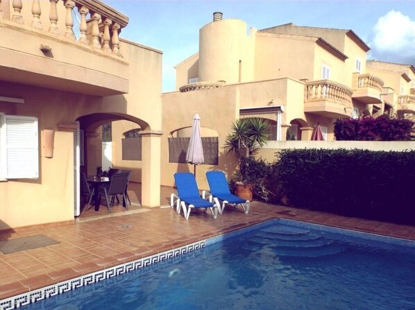 A swimming pool with lounge chairs, a table, and a covered area.