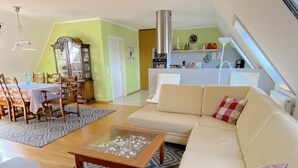 Un vaste espace de vie comprenant un canapé, une table à manger avec des chaises, une table basse en verre et une cuisine à l’arrière-plan.