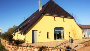 Un bâtiment jaune avec un toit foncé, un mur en pierre et un petit jardin.