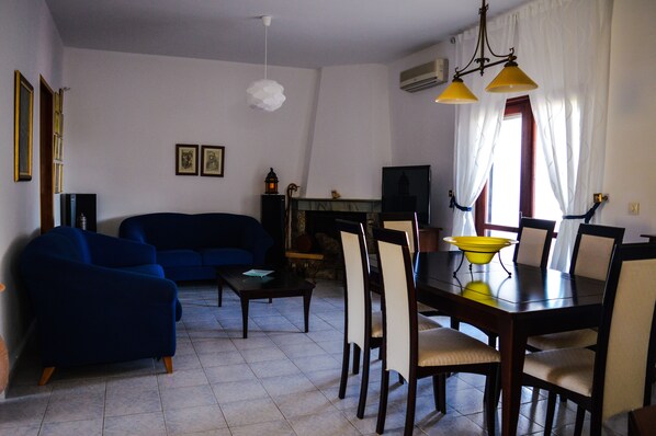 A living room with a blue sofa, a dining table with chairs, a fireplace, and a television.