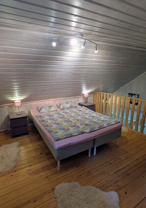 A bedroom with a bed, bedside lamps, a wooden floor, and a railing. - Close to nature, family-friendly holiday home with sauna and trampoline (Norrtälje)