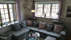 A modern living room with a grey sectional sofa, a glass coffee table, and a view through large windows.
