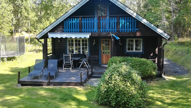 A wooden cabin with a porch, two chairs, a table, and a trampoline.
