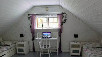 Een kamer met schuine plafonds, een bureau met computer, twee nachtkastjes, een stoel en een bed met bloemenprint beddengoed.