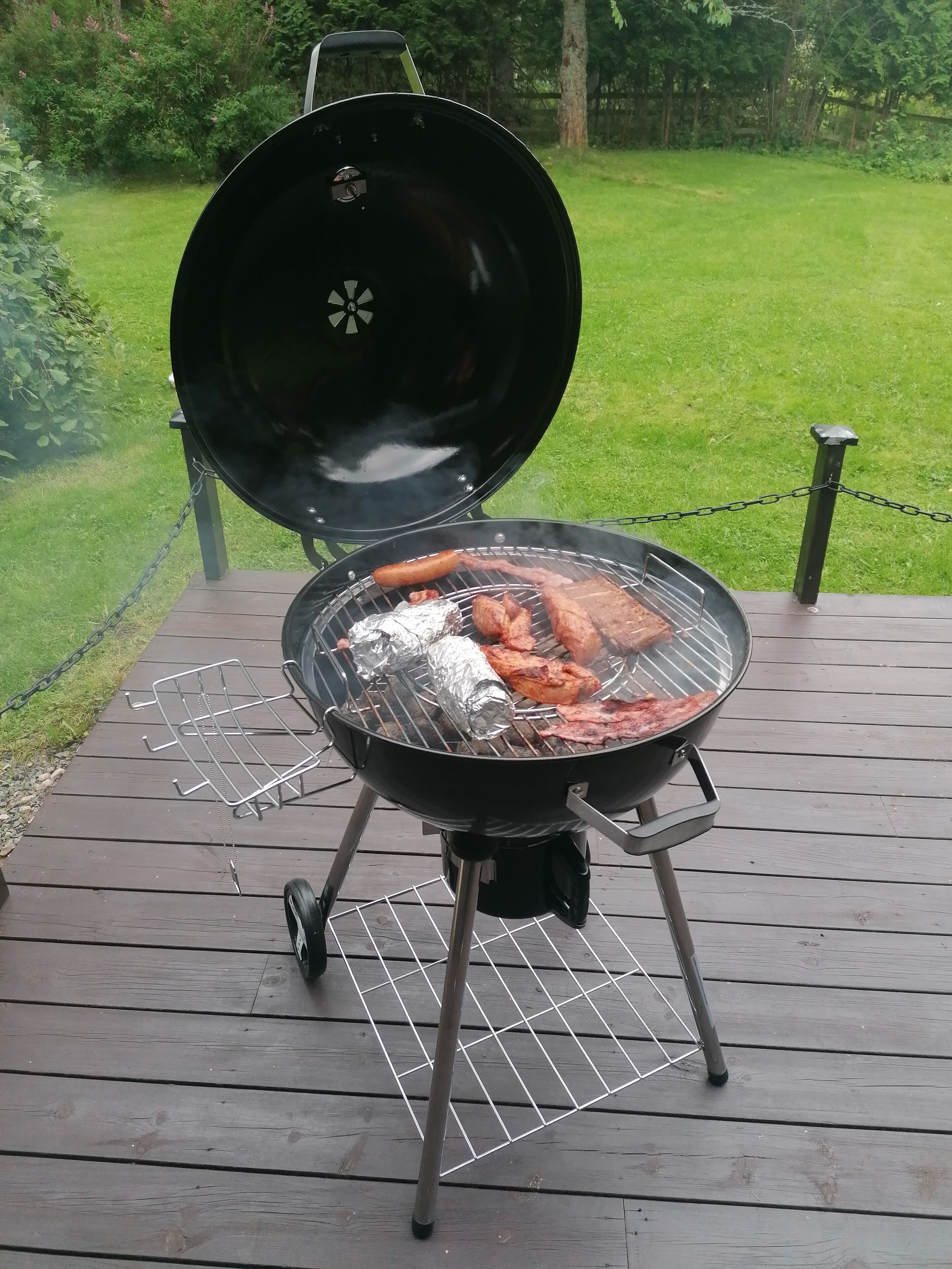 A portable grill on a wooden deck with a chain barrier.