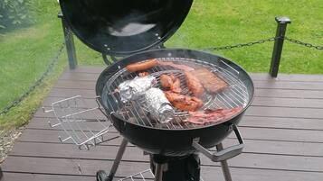 A portable grill on a wooden deck with a chain barrier.