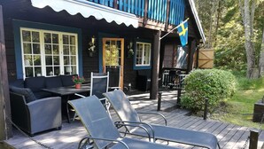 A wooden deck with lounge chairs and a table, a covered seating area with a sofa, and a flag.