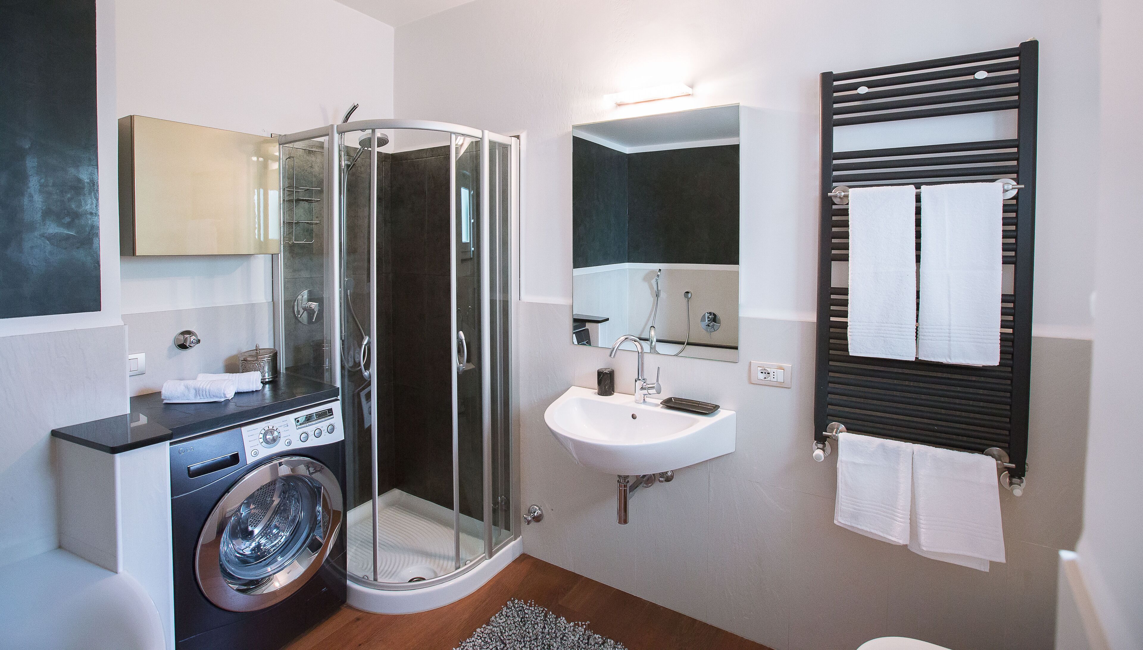 A modern bathroom with a glass-enclosed shower, a sink, a mirror, a towel rack, and a washing machine.