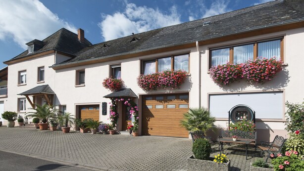 A two-story building with a wooden garage door, flower boxes, and potted plants. - Holiday Apartment "Pharmacy" with Weinbergblick (Trittenheim)