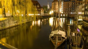 Un río tranquilo con barcos amarrados, edificios históricos y una torre destacada al fondo.