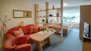 Een gezellige woonkamer met een rode bank, een houten salontafel en een televisie op een houten dressoir.
