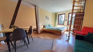 A cozy living room with a bed, a dining area, and a staircase.