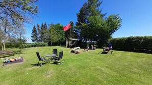 A grassy backyard with a picnic table, chairs, a swing, and a red flag.