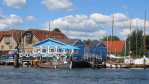 A waterfront area with several small blue buildings, likely serving as boathouses or guest accommodations, docked alongside the water. - Spacious apartment for two (Stoltebuell)